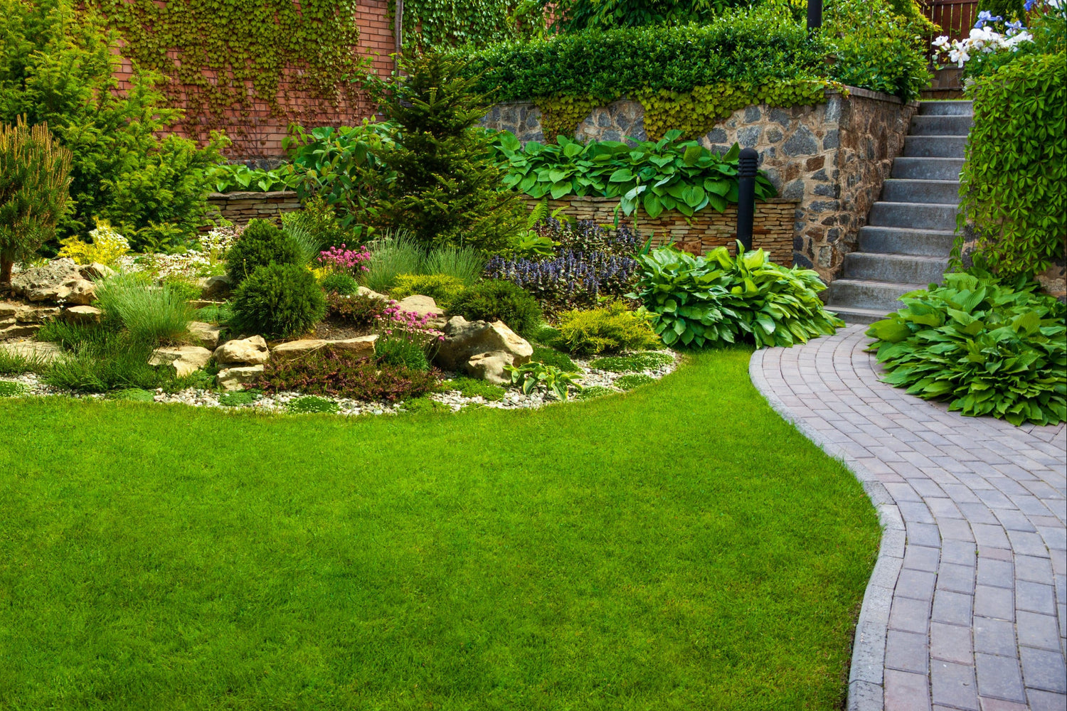 Landscape and hardscape design featuring curved paver walkway, stone retaining wall, and lush garden planting in Minneapolis