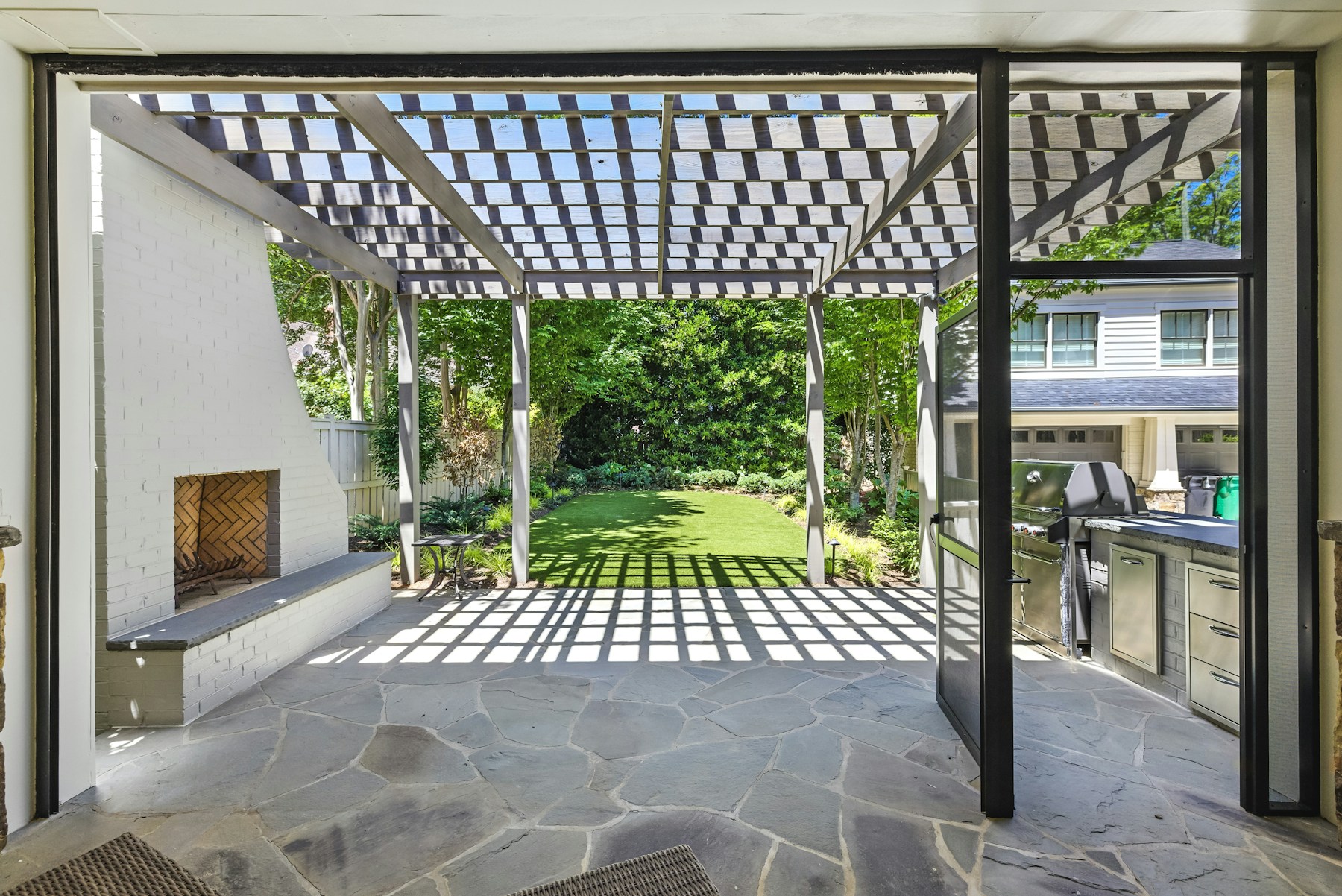 Upscale landscaped patio with stonework, pergola, outdoor kitchen, fireplace, and garden view